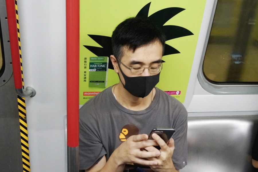 A man on his phone in the Hong Kong MTR sits in front of a picture which makes it appear as though he has Dragon Ball-Z character Goku’s hairstyle.  