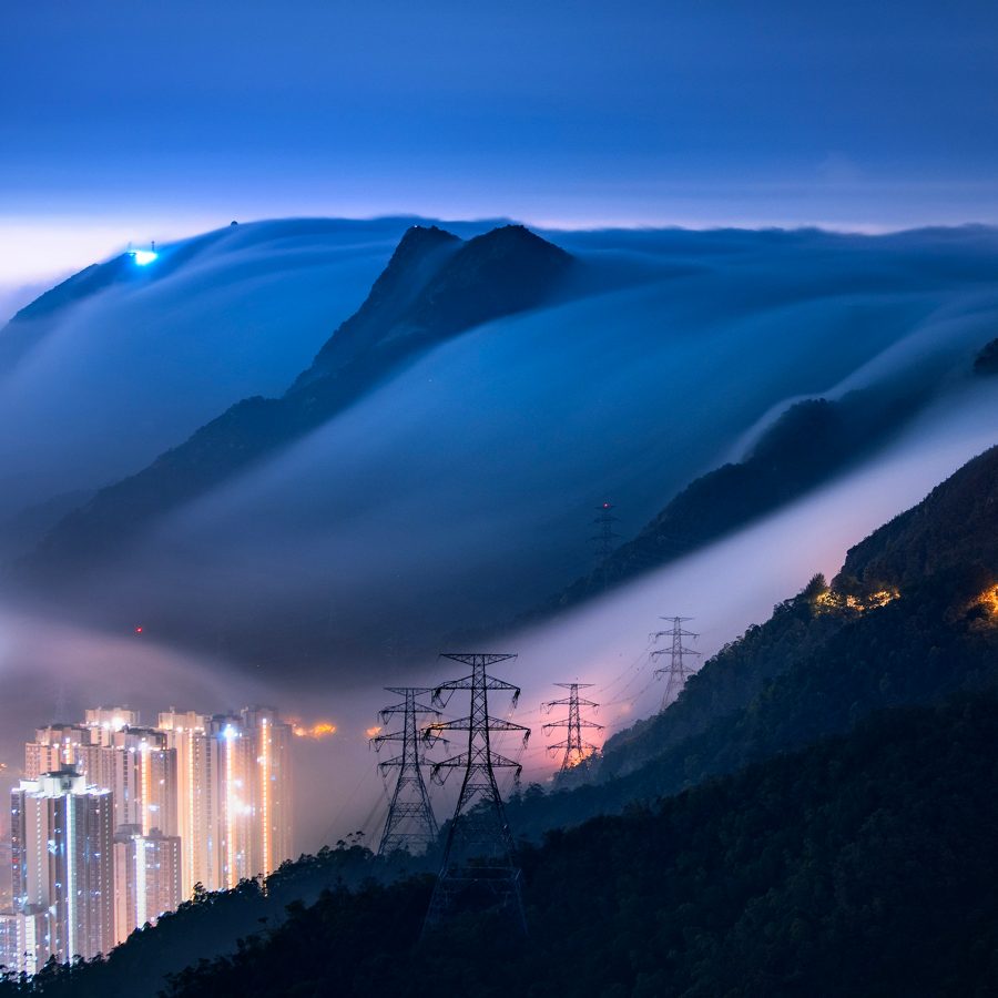 Mist rolling over the mountains and down towards buildings in Hong Kong.