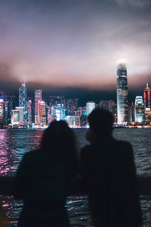 Two people stand silhouetted against the misty Hong Kong skyline,.