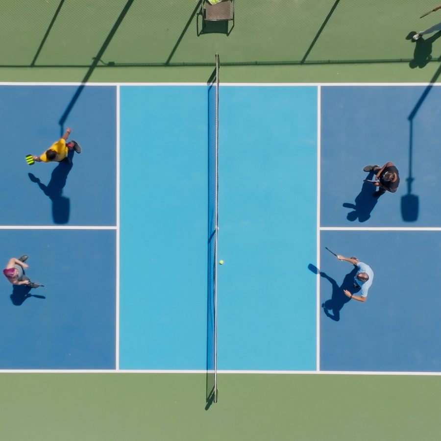 A top down view of a pickleball court shows four players playing the racket sport.