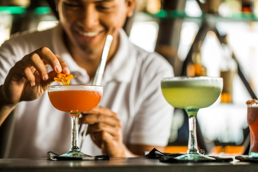 A smiling bartender garnishes an orange drink with a flower. 