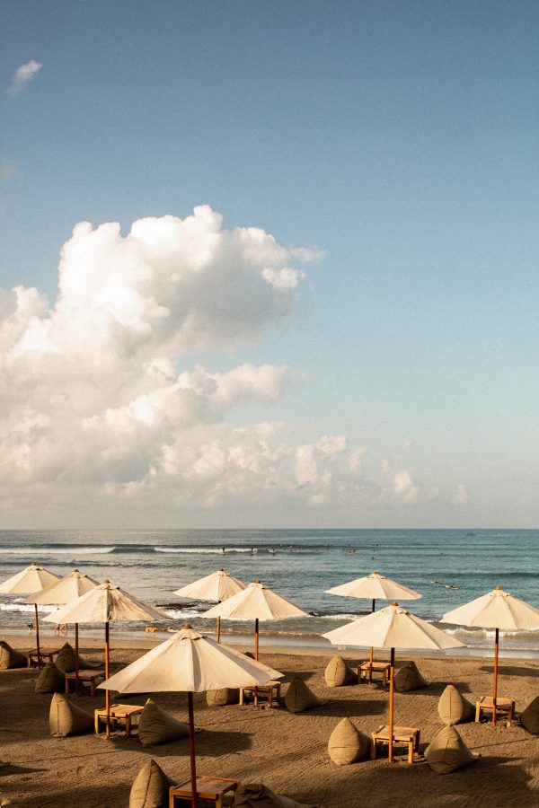 Umbrellas stand over lounge chairs on the beach in front of a quiet sea.
