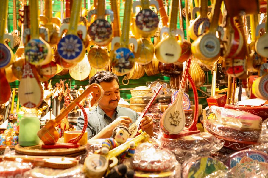 A man holding a dutar in a stall selling colourful instruments at Xinjiang International Grand Bazaar.