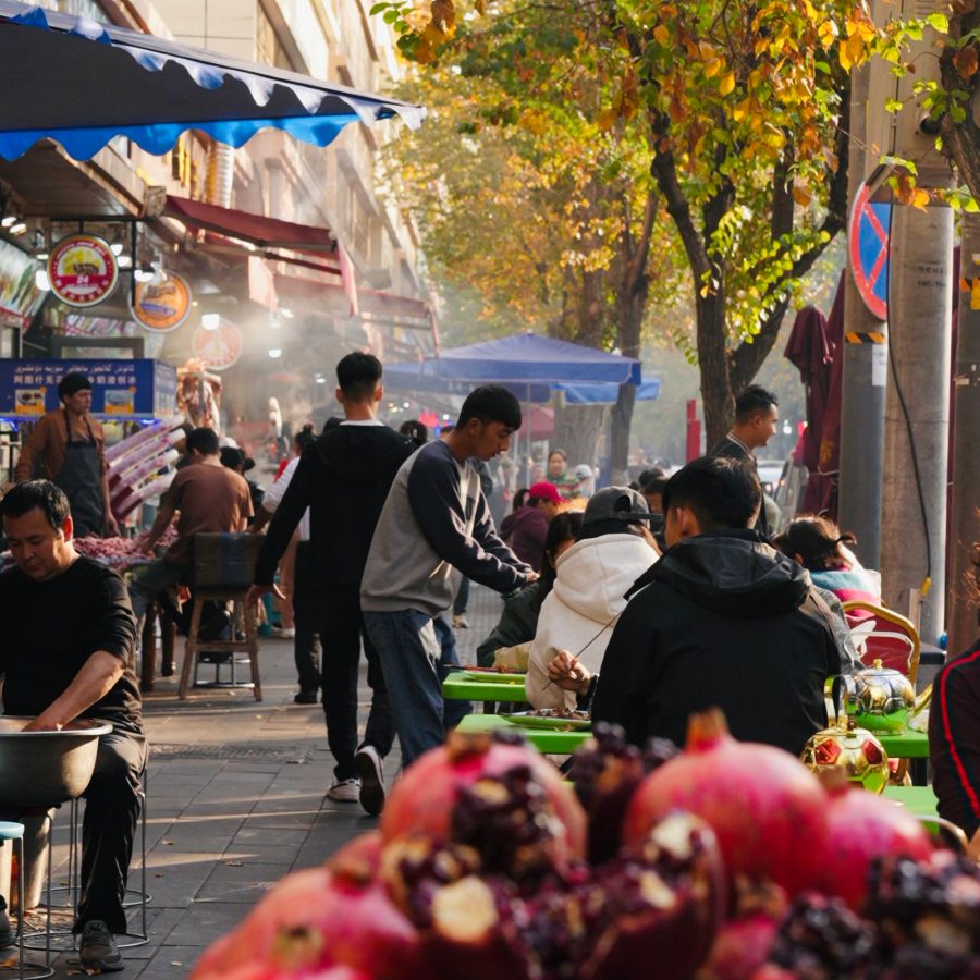 People walking on the tree-lined Hotan Street while restaurant staff serve patrons sitting at outdoor tables.
