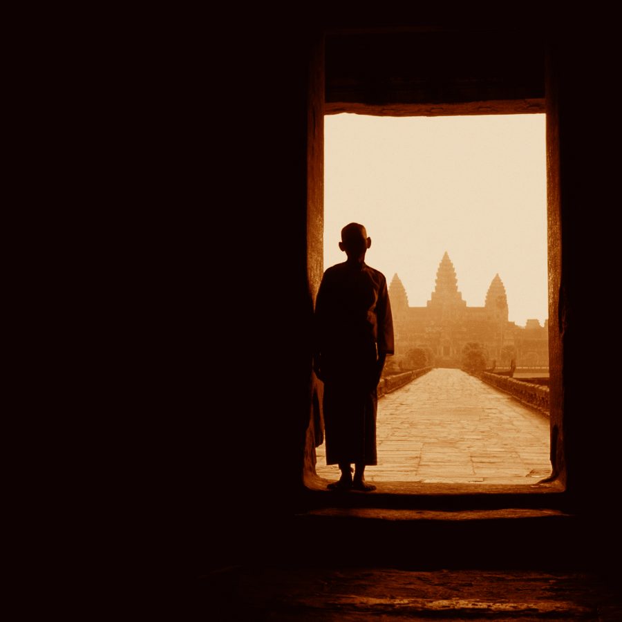 A monk stands in a doorway at Angkor Wat with a view of the temple spires in the distance.
