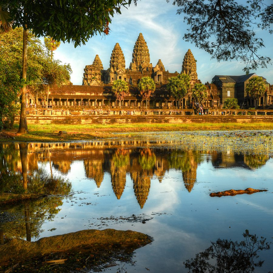 Angkor Wat surrounded by trees, with a body of water in front.