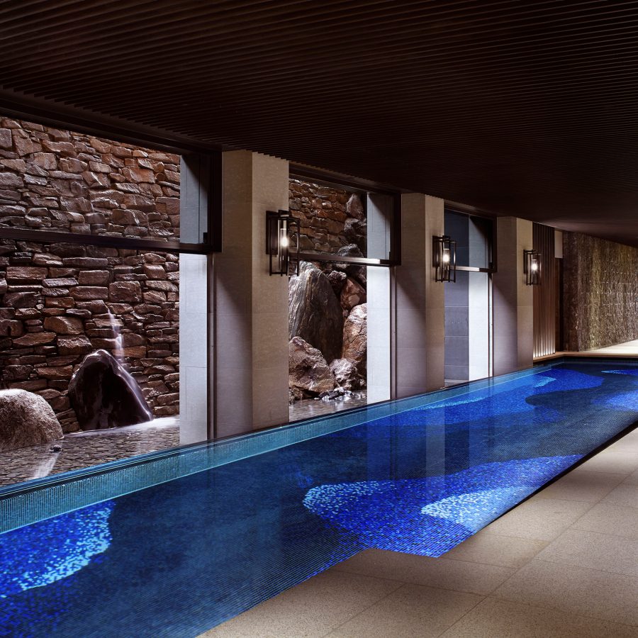 An indoor pool glows blue next to a row of lounge chairs at The Ritz-Carlton, Kyoto. 