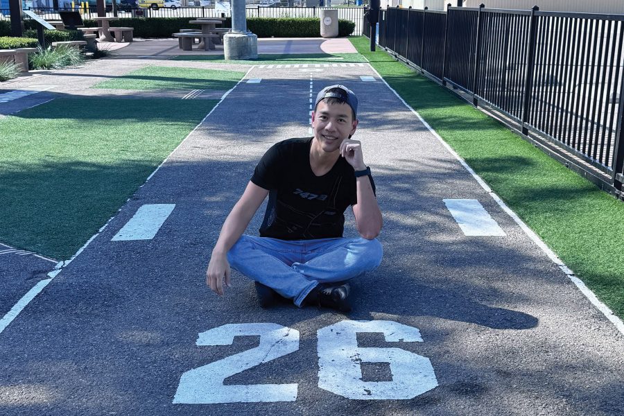 William Tsai smiles while sitting in a garden designed to a resemble a miniature airport runway.