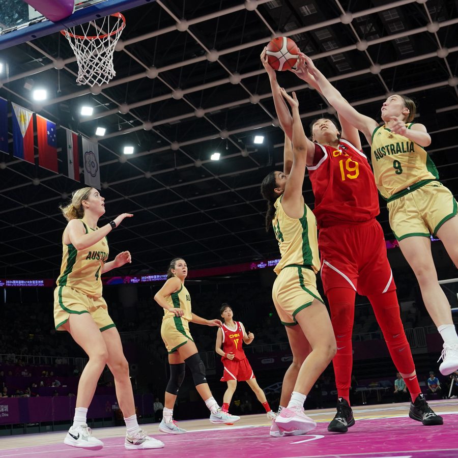 Members of the Chinese and Australian women’s basketball team reach for a ball near the hoop.