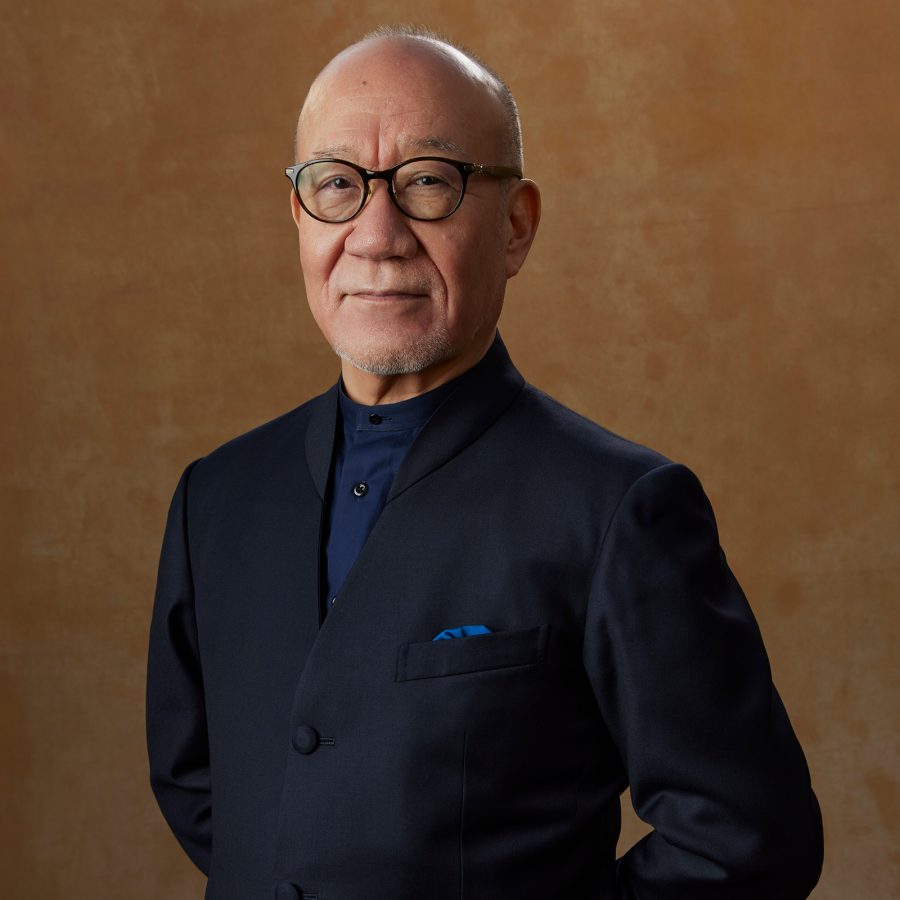 Joe Hisaishi takes a photo in front of a brown background.  