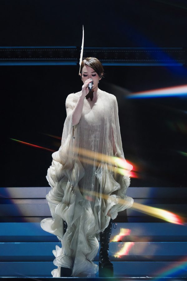 Sandy Lam performs on stage in a white flowy dress.