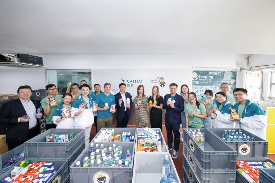 Cathay’s Chief Customer and Commercial Officer Lavinia Lau and General Manager Corporate Affairs Andy Wong with Feeding Hong Kong founder Gabrielle Kirstein OBE at an event to celebrate over 10 years of partnership between Cathay   and Feeding Hong Kong. Crates of packaged beverages are in front of them.