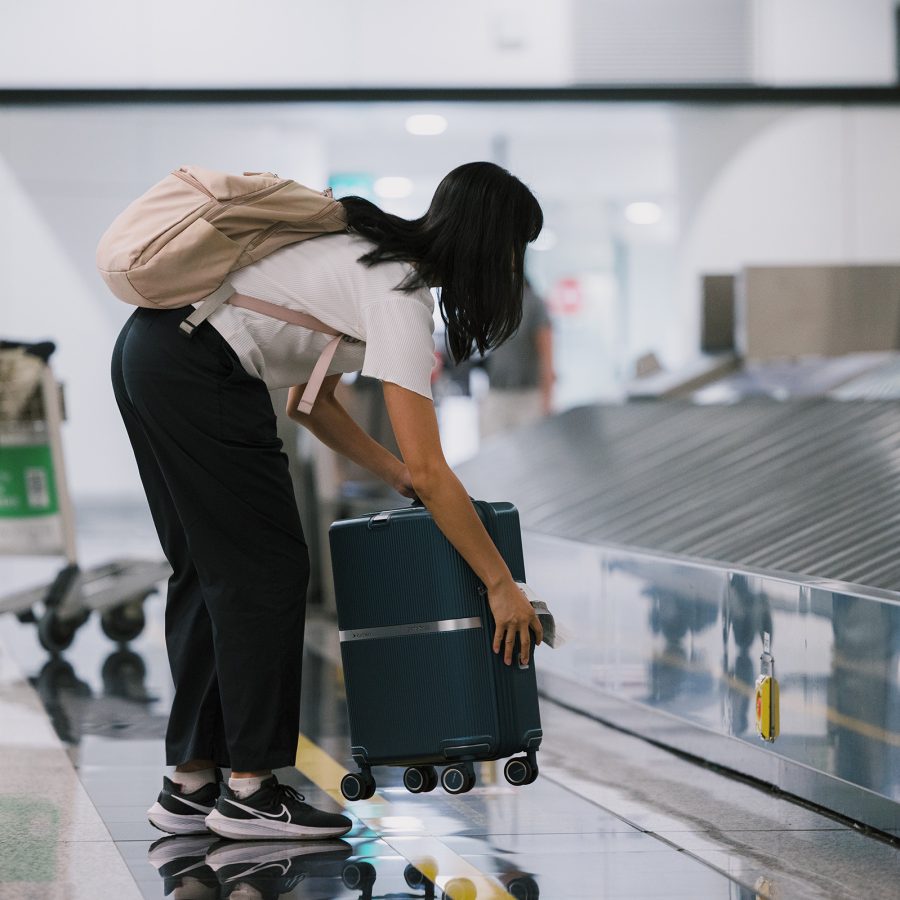 Girl bends over to pick up a grey luggage at the baggage claim conveyor belt at HKIA