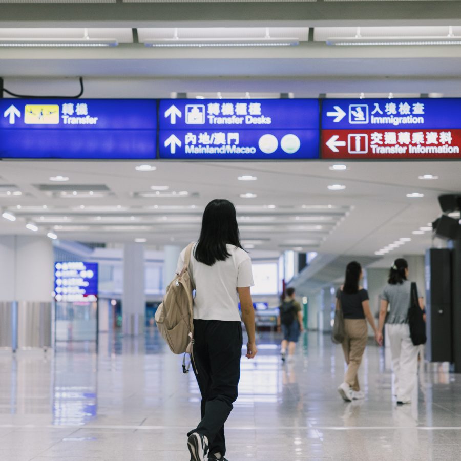 A girl walks through the transfer hall at HKIA with signboards overhead.