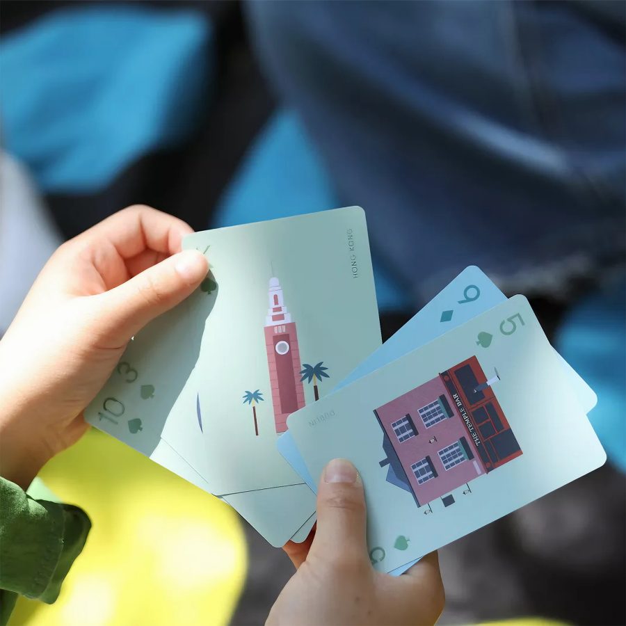 A young child holding a set of Cathay Pacific destination playing cards with images of various iconic landmarks around the world