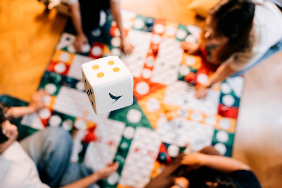A white dice with Cathay Pacific brushwing floating overhead while four friends play on a large foldable Cathay Pacific aviation chess mat