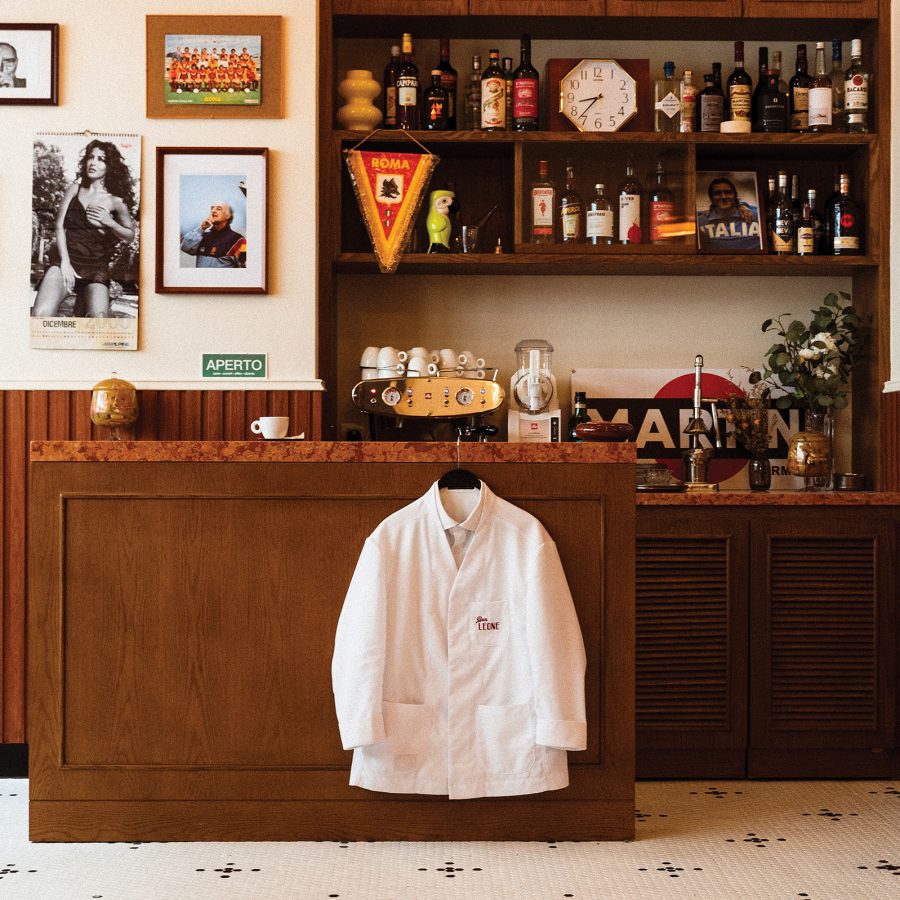 Interior view of Bar Leone in Hong Kong – with a bartender’s white jacket hanging from a small wooden bar, behind which there are bottles and objects from Italy, as well as photographs hanging on the wall.