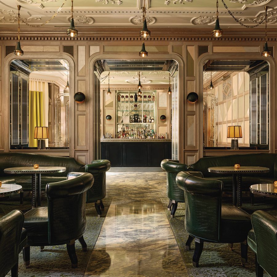 Interior view of The Connaught bar in London – with green leather armchairs, high ceilings decorated in an ornate style and an grand bar in the background