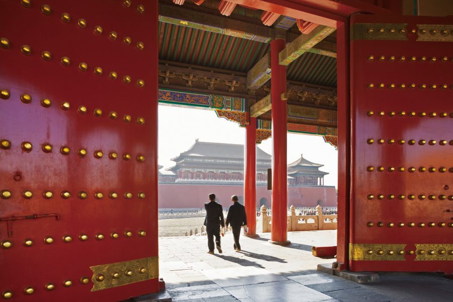 Two people walking through red doors of Forbidden City into the courtyard outside.