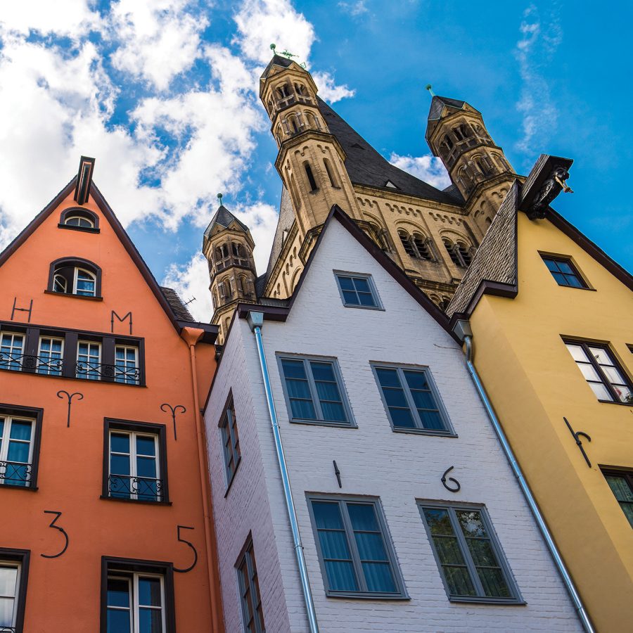 A Romanesque church rises behind three colourful townhouses in Cologne.