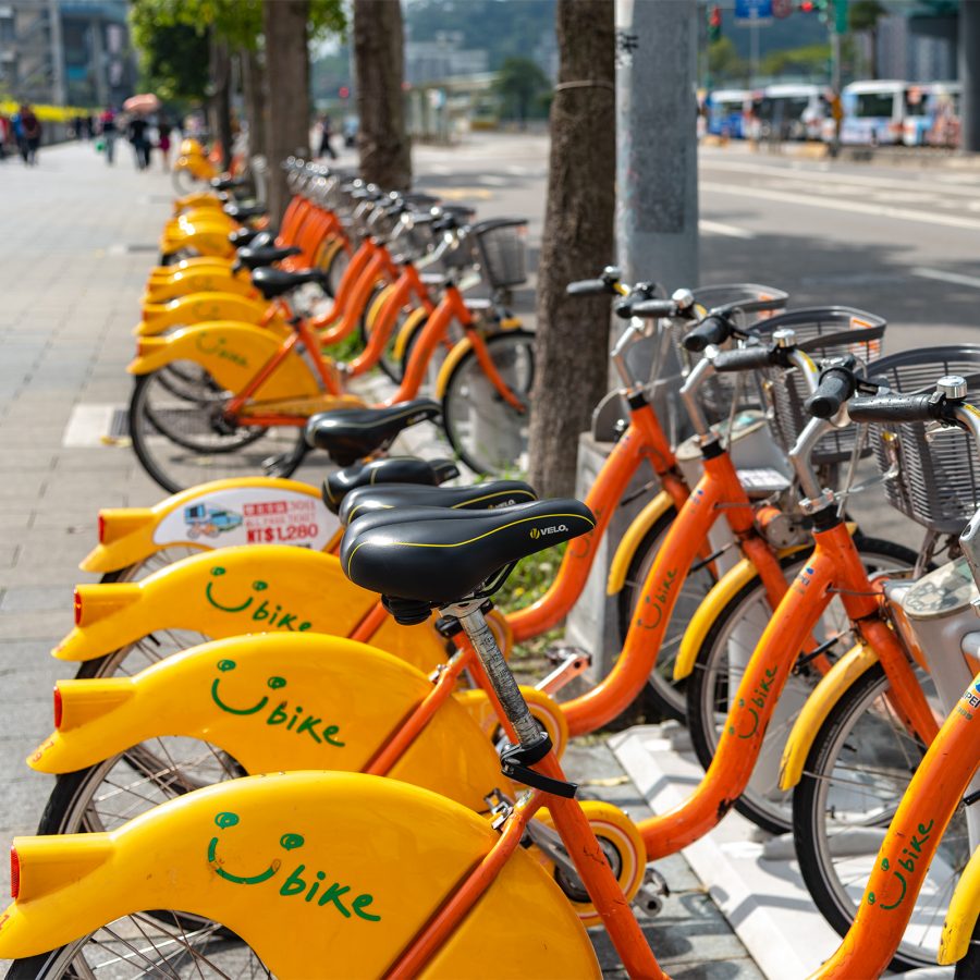 Rental bicycles are lined up in a neat row along the sidewalk.   