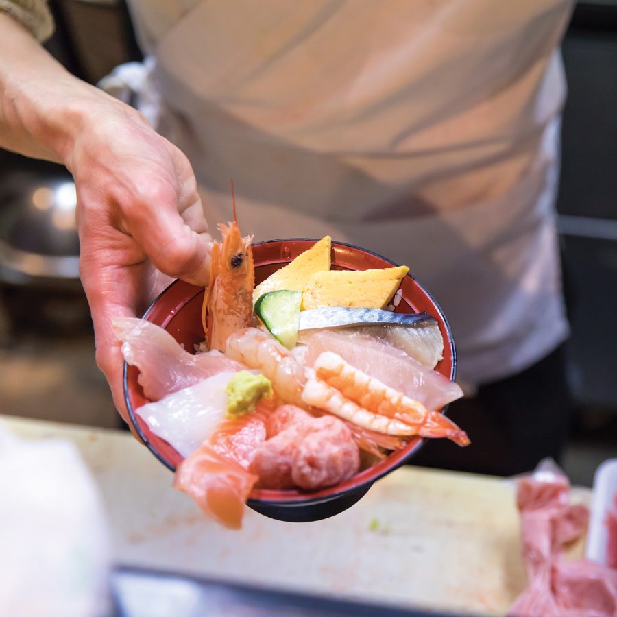 Close-up of a hand holding a sashimi don at Omicho Market. 