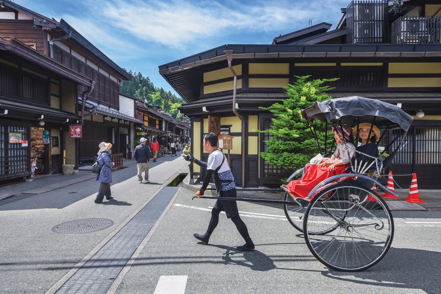 A man pushing a rickshaw with people on the traditional streets of Takayama.  