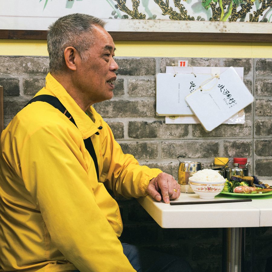 Ming Gor sits at a booth in his cha chaan teng Pei Ho Counterparts, chatting to someone sitting across from him.