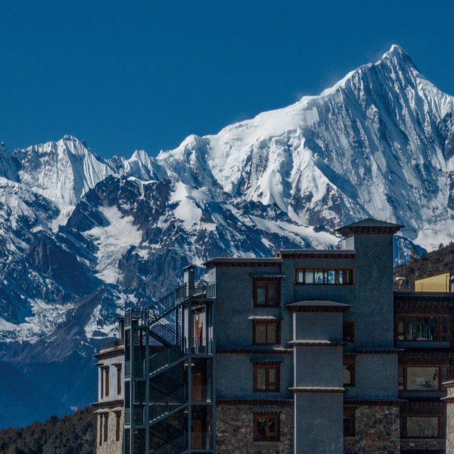 Exterior of Songtsam Meili Hotel with snow-capped mountains in the background.
