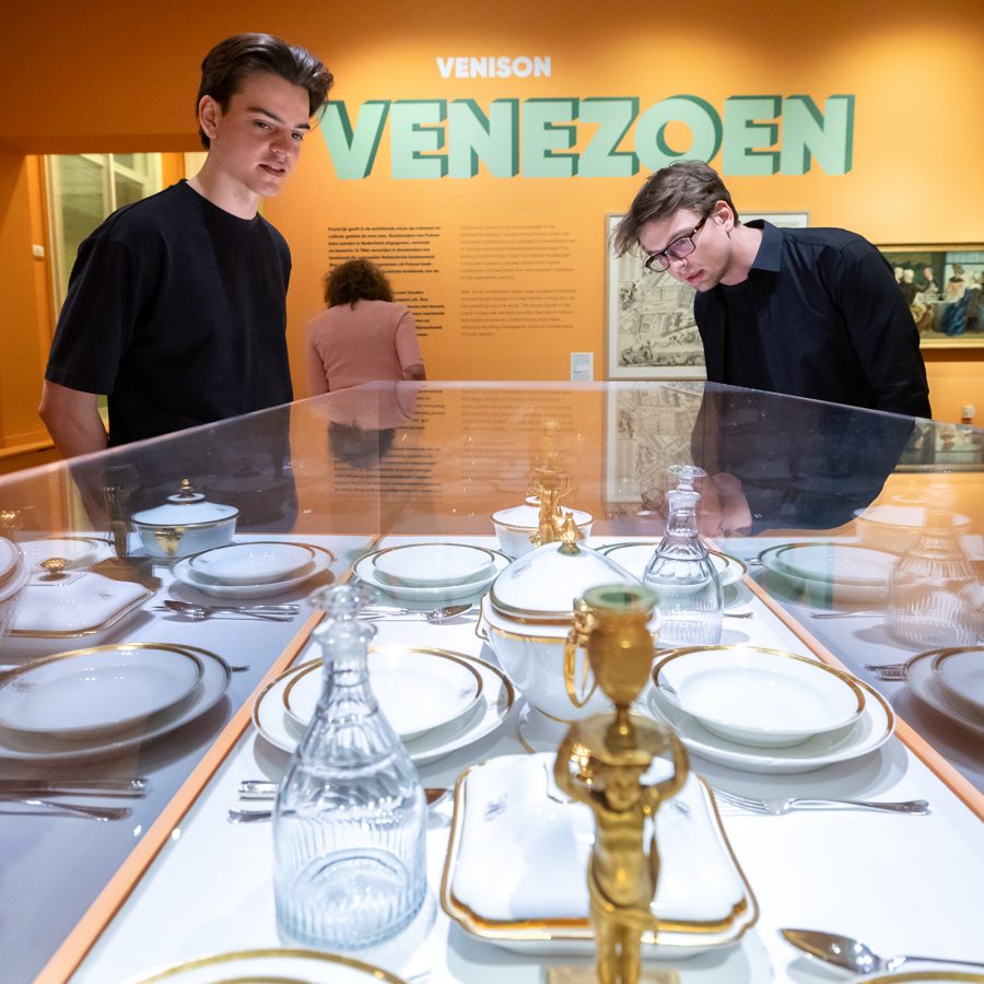 Two men looking through a glass box display of vintatage plates and tableware in a museum in Amsterdam, Netherlands