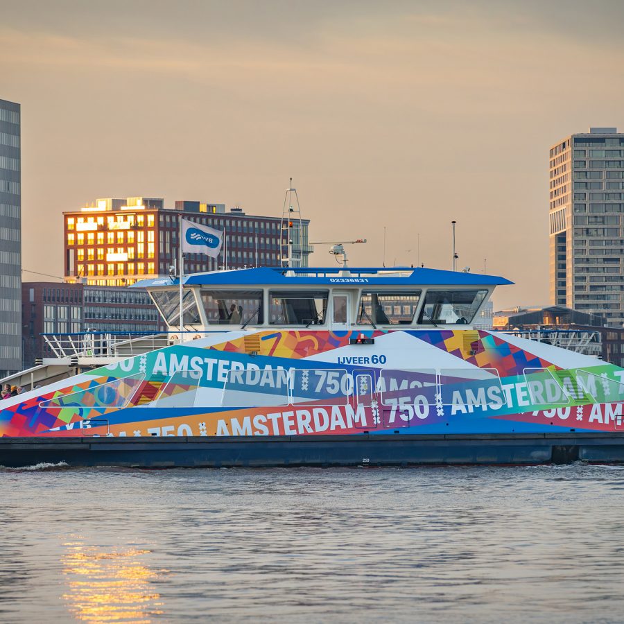 A boat decorated with colourful signs of Amsterdam National Celebration of 750 Years of Amsterdam with the skyline in the background
