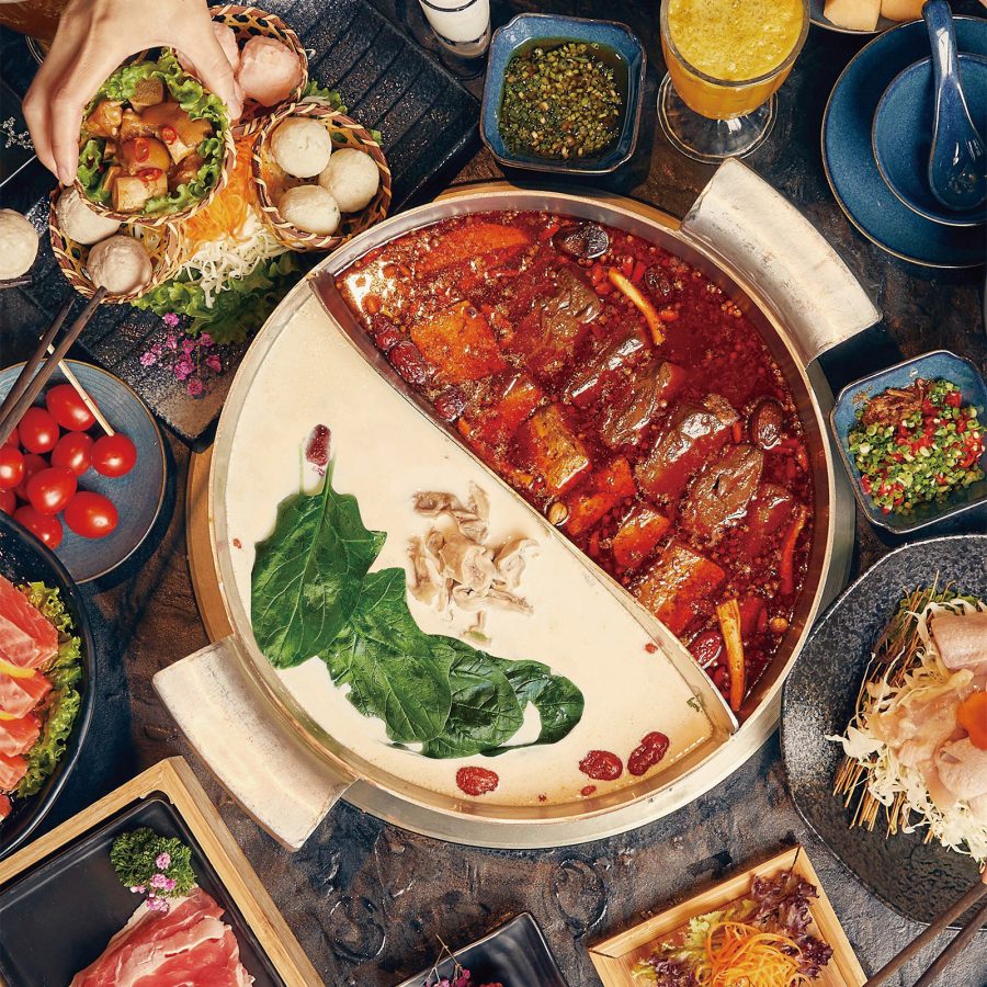 Flat lay family spread of two soups in a hot pot with various dishes around served at Coucou Hot Pot Tea Break