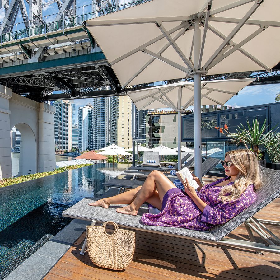 A woman reading on a lounge chair by the pool at Crystalbrook Vincent in Brisbane.