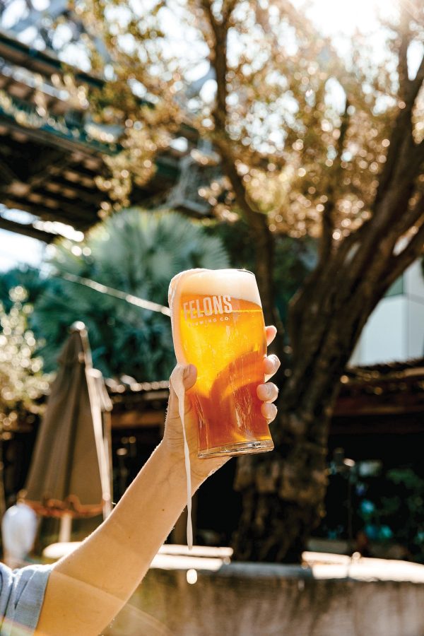 A hand holding a glass of beer outdoors at Felons Brewing Co in Brisbane.