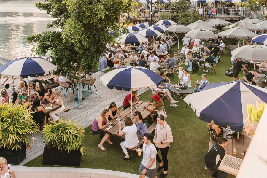 Many groups of people sitting outdoors around picnic tables with market umbrellas at Felons Brewing Co in Brisbane.