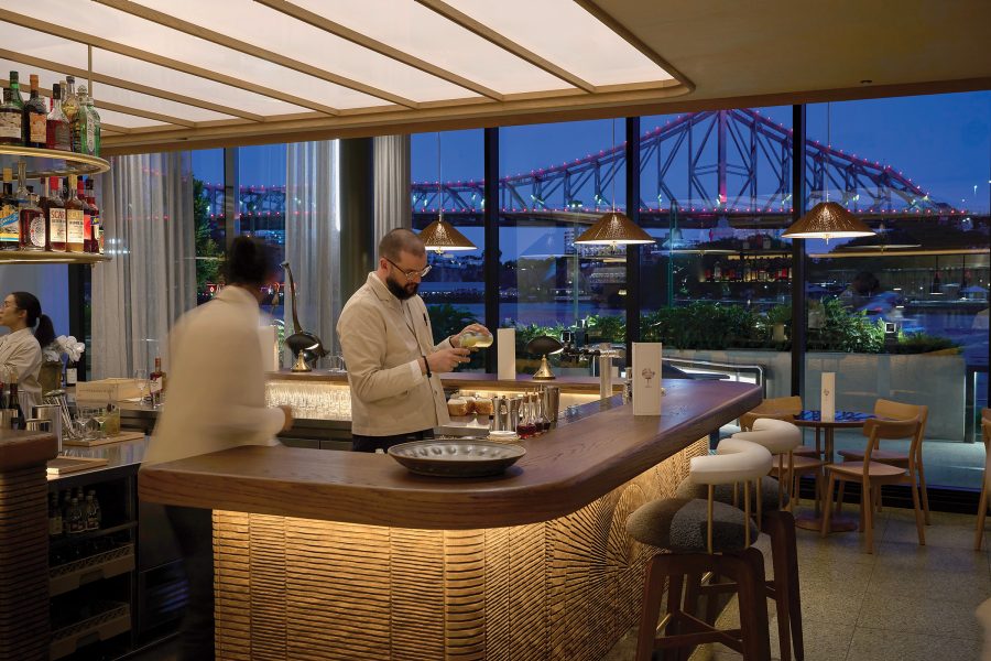 Two bartenders standing behind the bar at Supernormal in Brisbane, next to floor-to-ceiling windows with a view of Story Bridge.