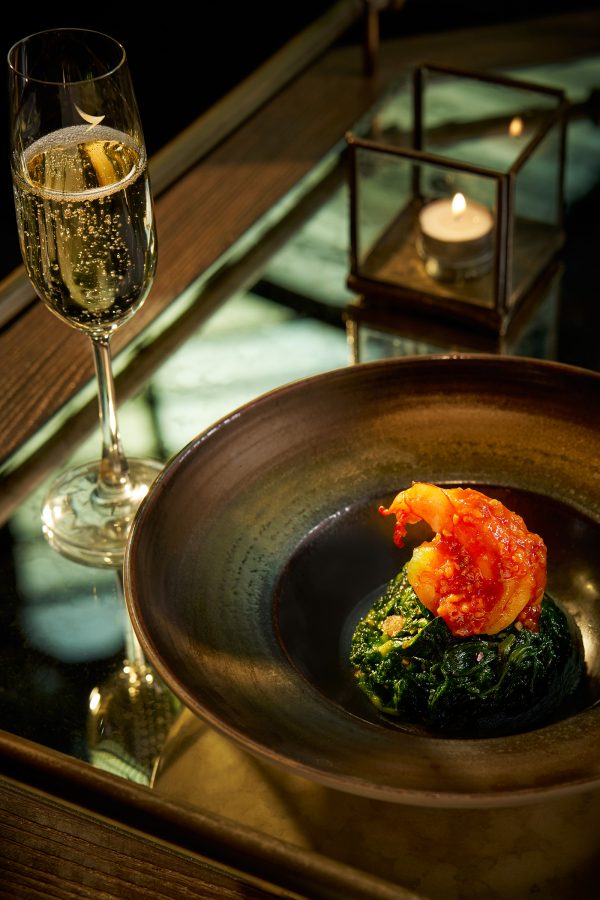 A bowl of food prepared by Mott 32 and a glass of champagne.