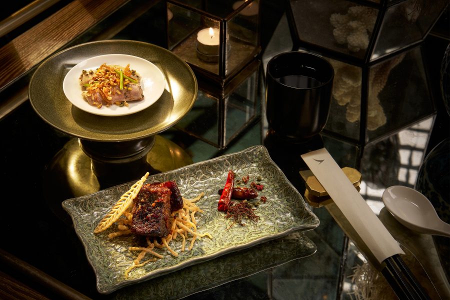 Two plates of Chinese food with Cathay cutlery and a cup of water.  