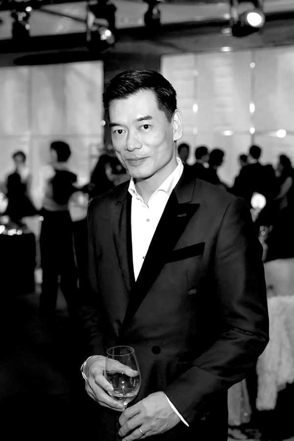 Xuan Mu, co-founder of Mott 32, in a suit holding a wine glass. 