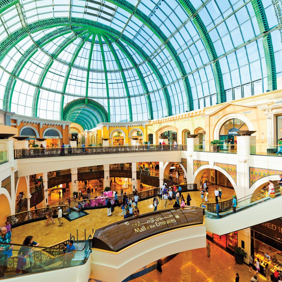 Interior view of the glass-ceilnged Mall of the Emirates, with shoppers on various floors perusing the designer shops.