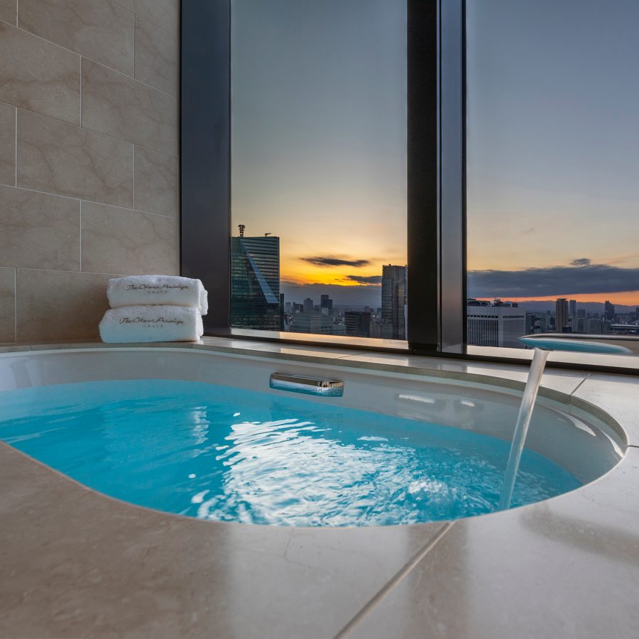 Water running into a large circular bath at The Okura Tokyo with a view of the Tokyo skyline at sunset.