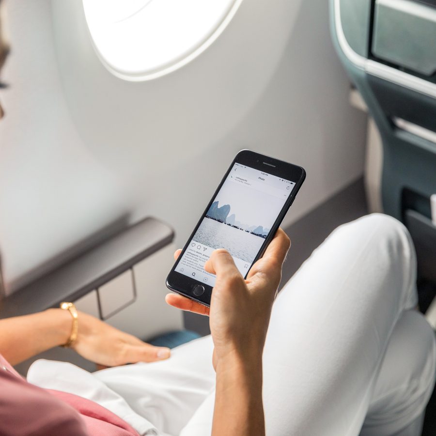 A woman looking at a Cathay Pacific Instagram post on her phone while on a Cathay Pacific flight.