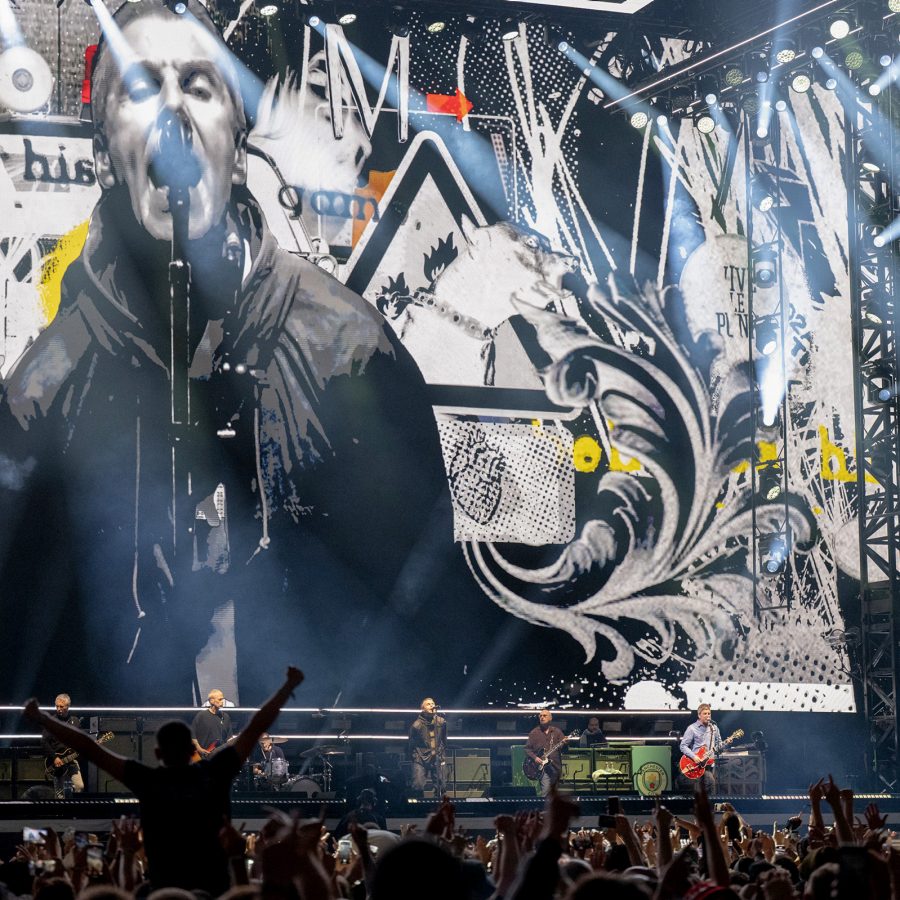 Oasis, scheduled to come to Seoul and Tokyo in 2025, are seen performing on stage as audience members below raise their arms in excitement.