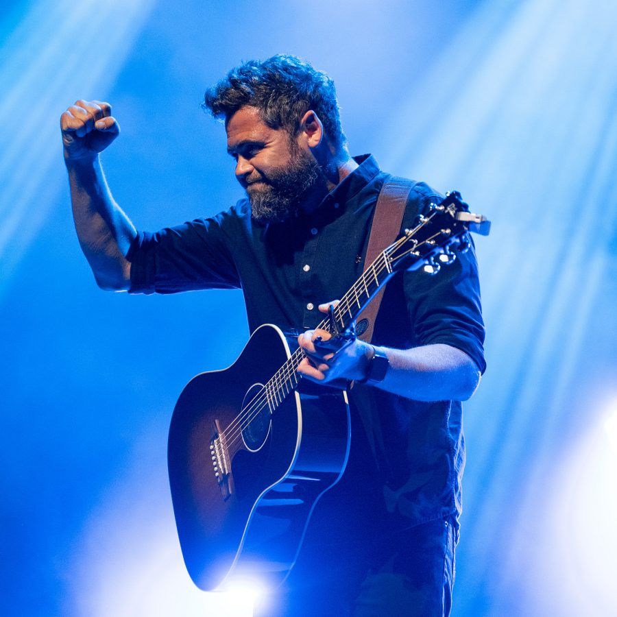 Passenger, who will visit Asia this winter, is seen in mid-performance as the stage behind him lights up blue. 