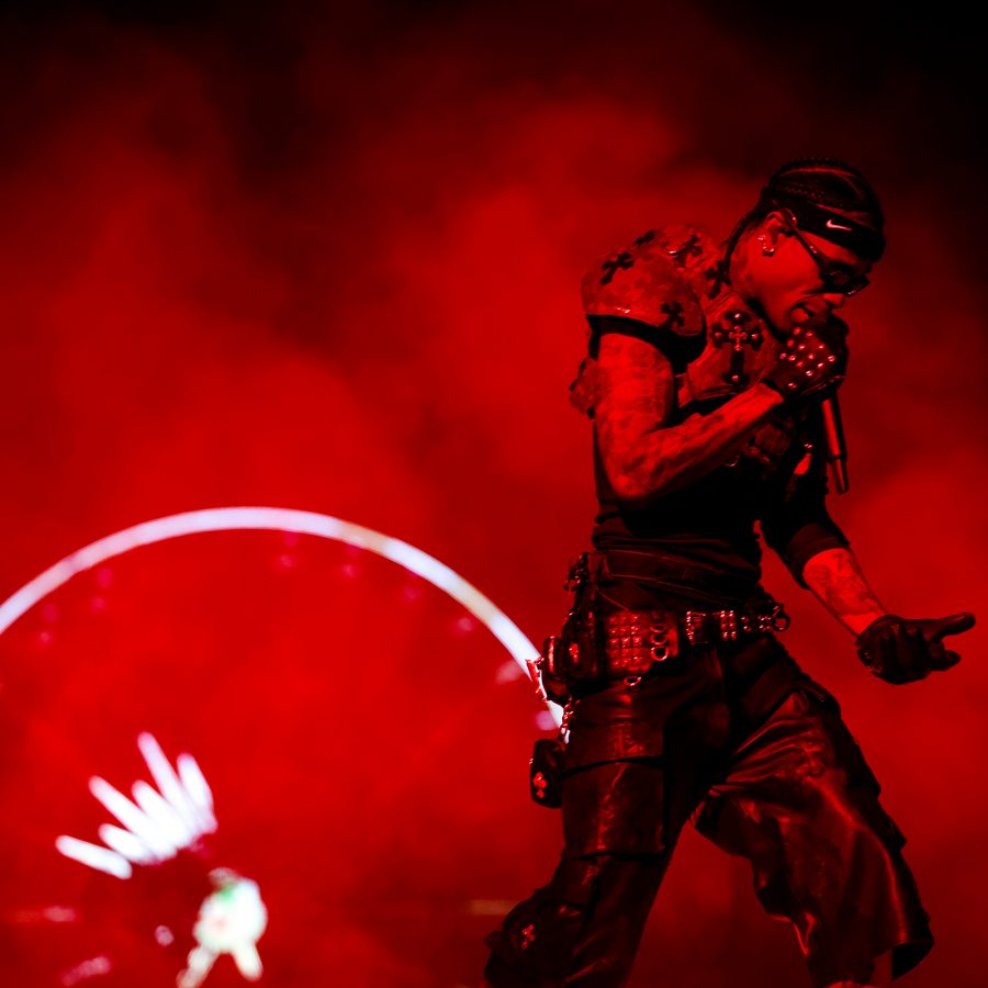Travis Scott sings with a mic in hand as the backdrop of the stage turns red.