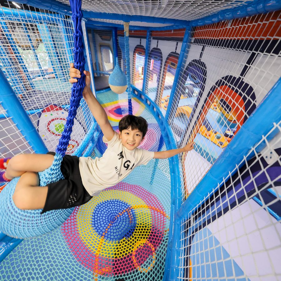 Interior view of a young child swinging on a large rope in Tiger’s Mojo Zone at Kiztopia. 