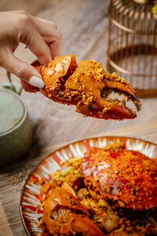 A closeup of a hand holding a large crab claw over a plate of whole fried crab, served at Canton House, Hong Kong.