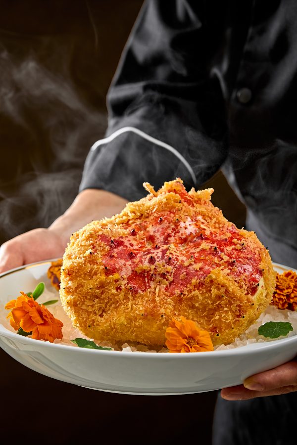 A closeup of hands holding a large plate of whole king crab with baked rice, served at China Tang, Hong Kong. 