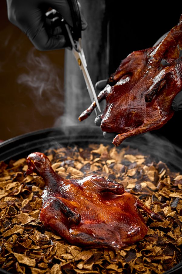 A closeup of a hand with scissors cutting the leg of a roasted pigeon over dried tangerine peel, served at China Tang, Hong Kong.