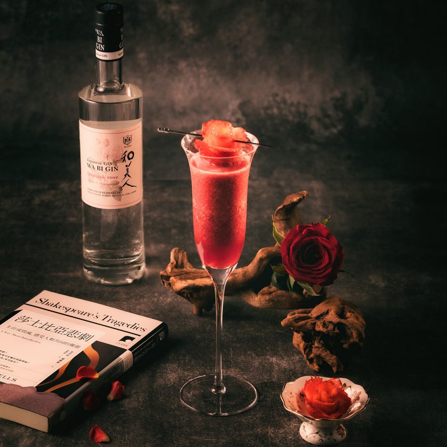 A tall glass of Sakura Shochutini cocktail with floral ingredients and a bottle of Akadori gin, served at Madara bar in Hong Kong.
